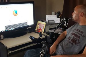 Man in wheelchair using a puff/blow device to control a computer