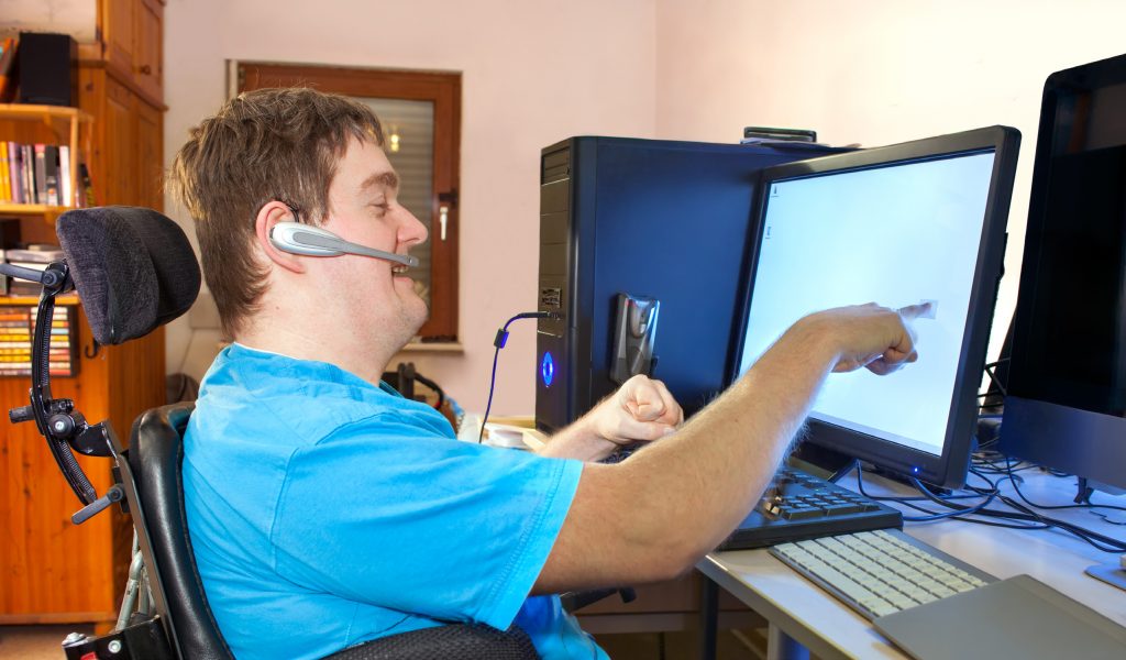 Man in wheelchair with headset on smiling and pointing at computer screen