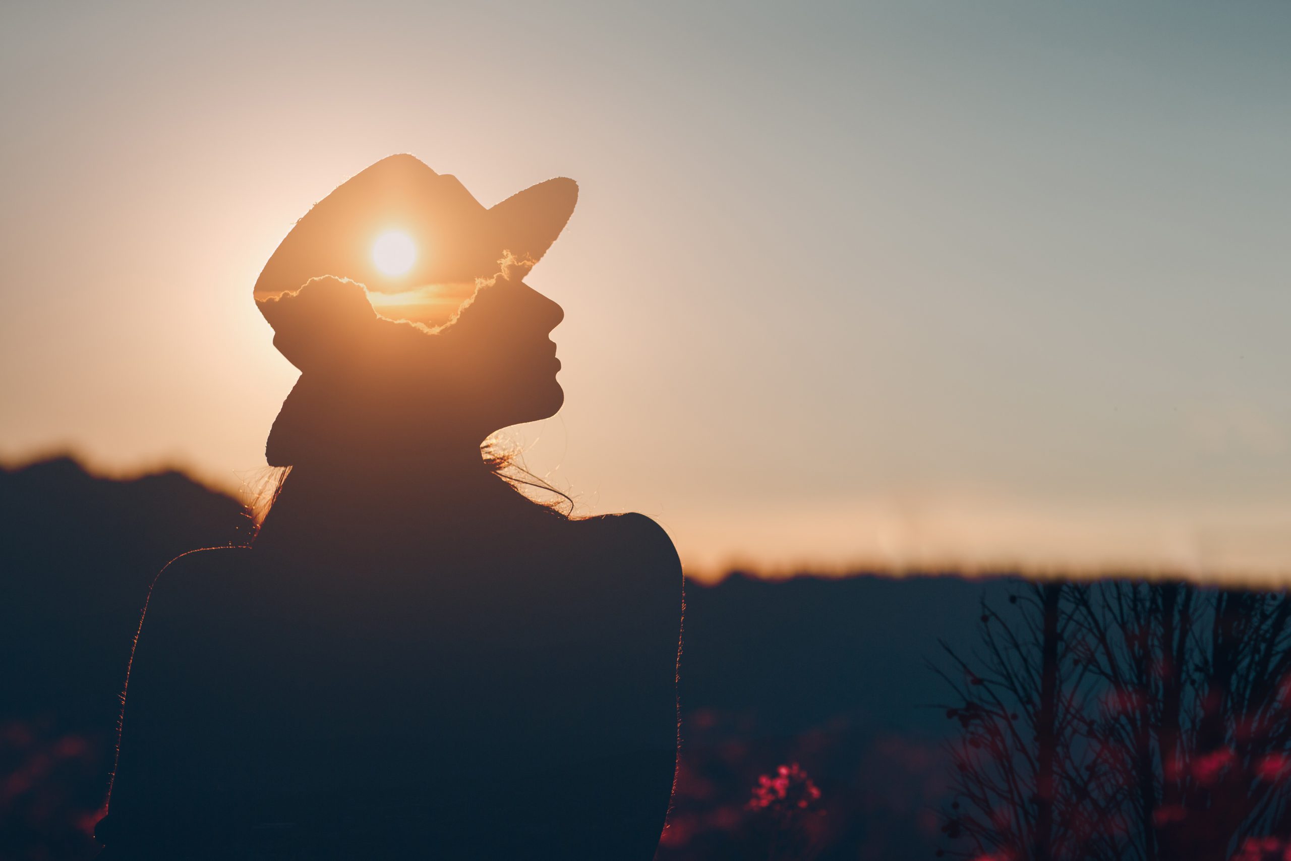 Silhouette of woman wearing a hat. The sun is shining through the hat, evoking an image of mental wellbeing.